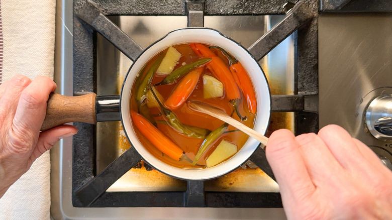 Stirring hot chiles, ginger root, honey and vinegar in small saucepan on stovetop with wooden spoon