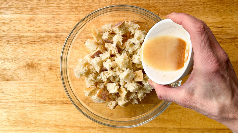 Pouring garlic butter onto bread cubes in glass bowl on cutting board