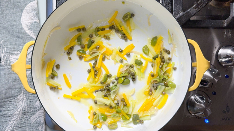 Green olives, capers, yellow bell pepper, and fennel in pot on stovetop