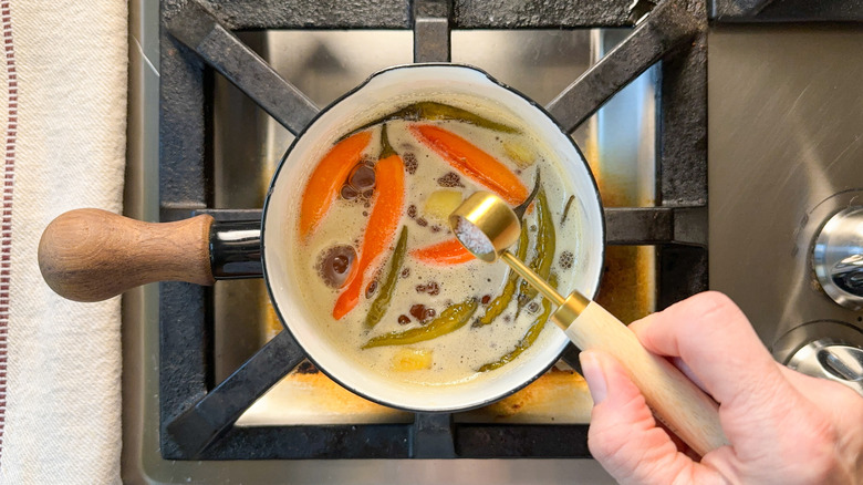 Adding salt to hot honey with chiles and ginger root in small saucepan on stovetop