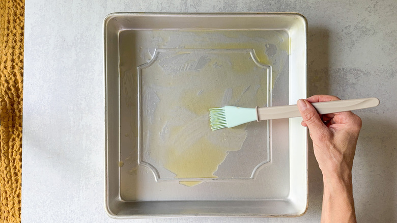 Coating a square baking pan with truffle oil using a pastry brush