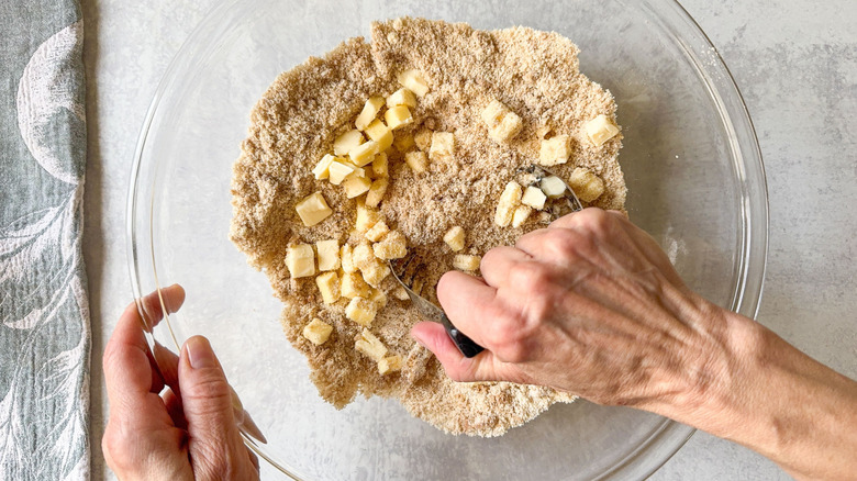 Mixing cold butter chunks into cobbler topping dry ingredients with pastry cutter in glass bowl