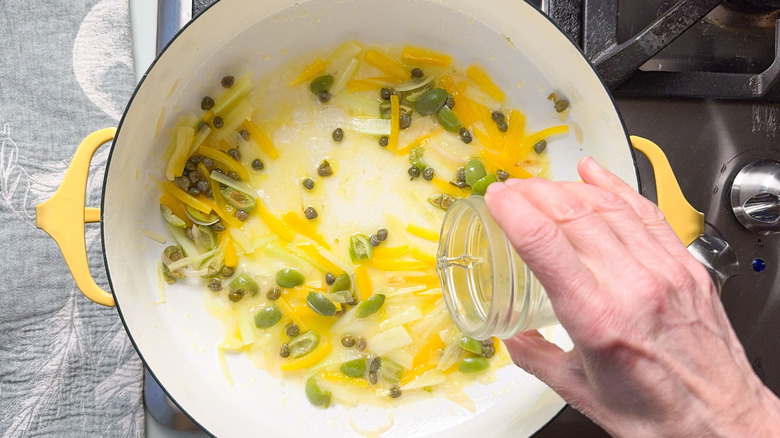 Adding white wine to green olives, capers, and yellow bell pepper in pot on stovetop