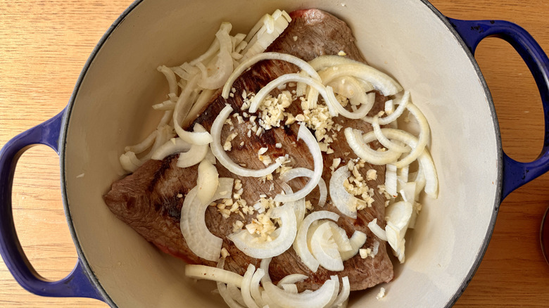 Onions and garlic over brisket in Dutch oven