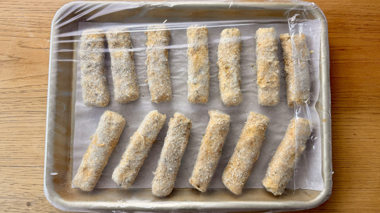 breaded cheese sticks in a plastic-wrapped baking pan