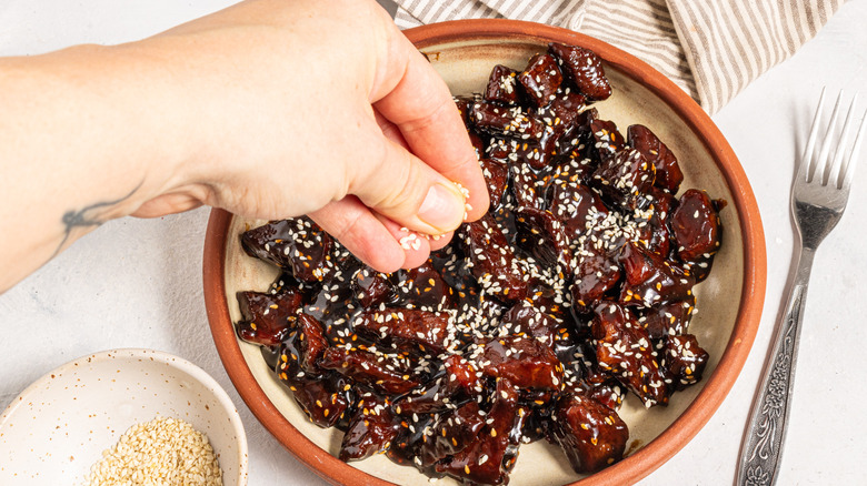 Sprinkling sesame seeds over a plate with sticky soy steak bites