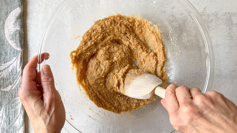Mixing gluten-free peach cobbler topping in glass bowl with wooden spoon