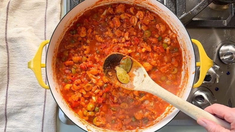 Removing bay leaves from romesco-y sauce in pot on stovetop with wooden spoon