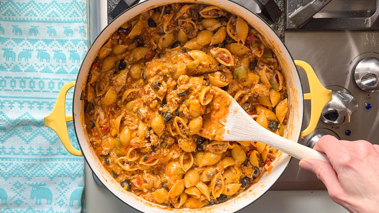 Stirring black olives and cheese into 1-pot turkey taco pasta with wooden spoon