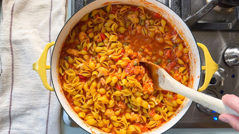 Stirring shell pasta into romesco-y sauce with tuna in pot on stovetop