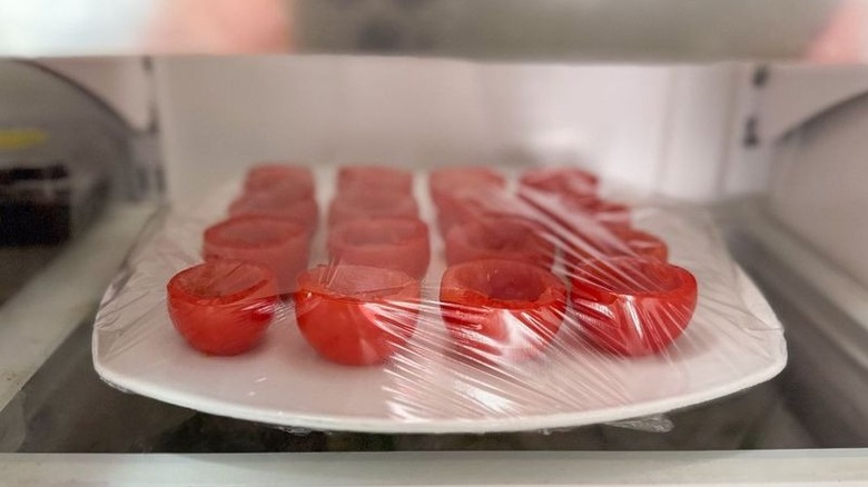 Hollowed-out tomato cups wrapped in plastic on plate in refrigerator
