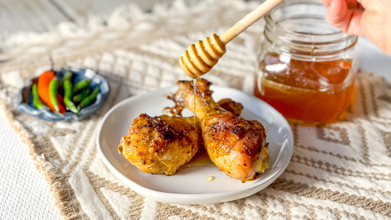 Drizzling homemade hot honey over chicken drumsticks on plate with red and green chiles