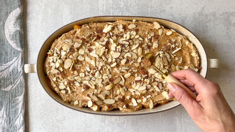 Sprinkling sliced almonds and turbinado sugar on top of gluten-free peach cobbler before baking