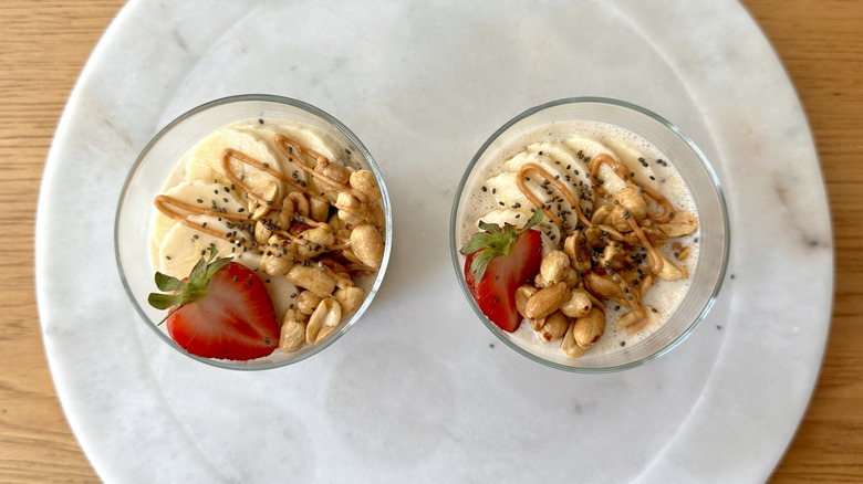 Overnight oats in jars topped with bananas, strawberry slice, peanuts, and peanut butter drizzle