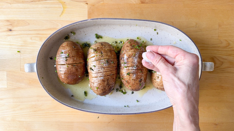 Sprinkling salt onto basted Hasselback potatoes