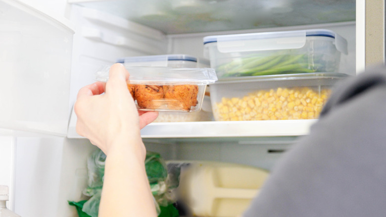 Person placing a plastic container of food onto a shelf in the refrigerator
