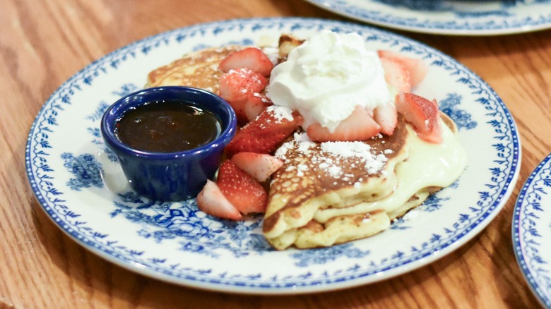A blue plate with stuffed pancakes with strawberries and whipped cream on top