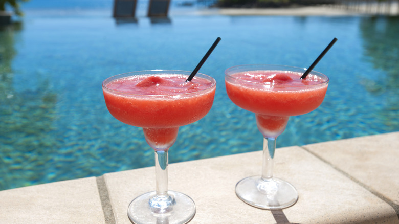 Two pink blended drinks sitting poolside