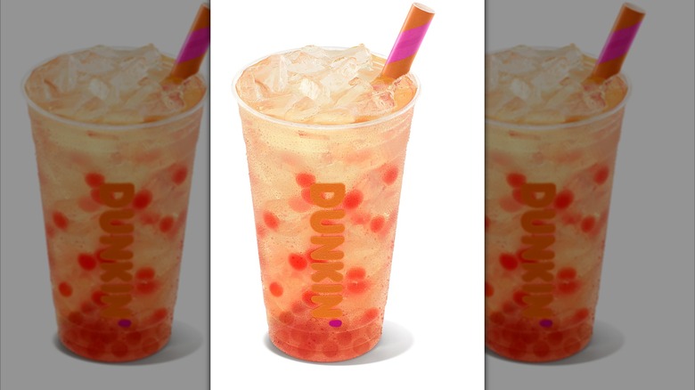 A glass of Dunkin' Strawberry Popping Bubbles in Lemonade with a pink and orange striped straw