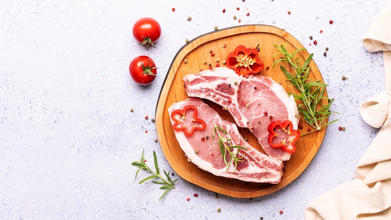 Raw pork chops on wooden board with garnish