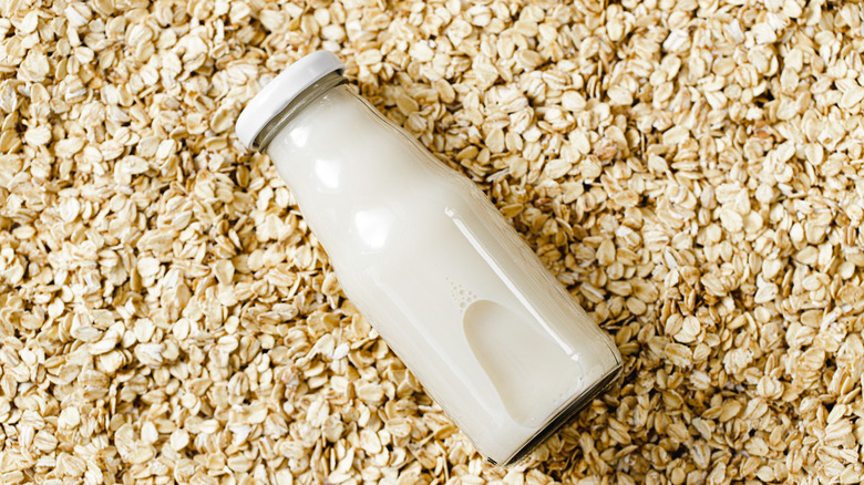 Glass bottle of oat milk on a background of oats
