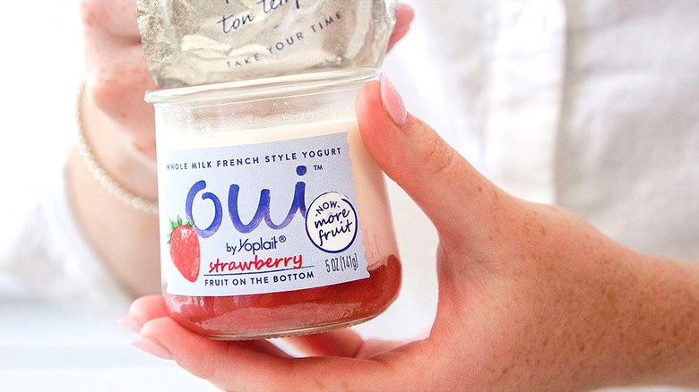 Hand holding a jar of Oui by Yoplait strawberry flavored yogurt