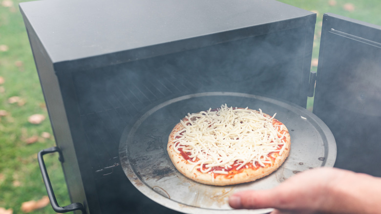 Loading pizza into a smoking oven outdoors