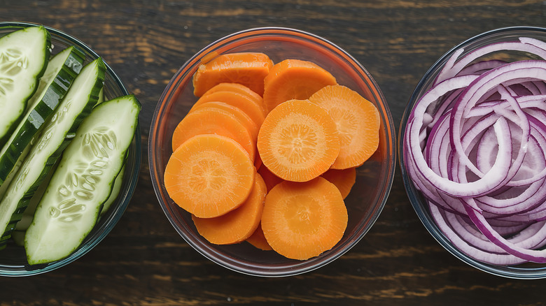 A photo of bowls contain sliced cucumbers, carrot slices, and thinly sliced red onions