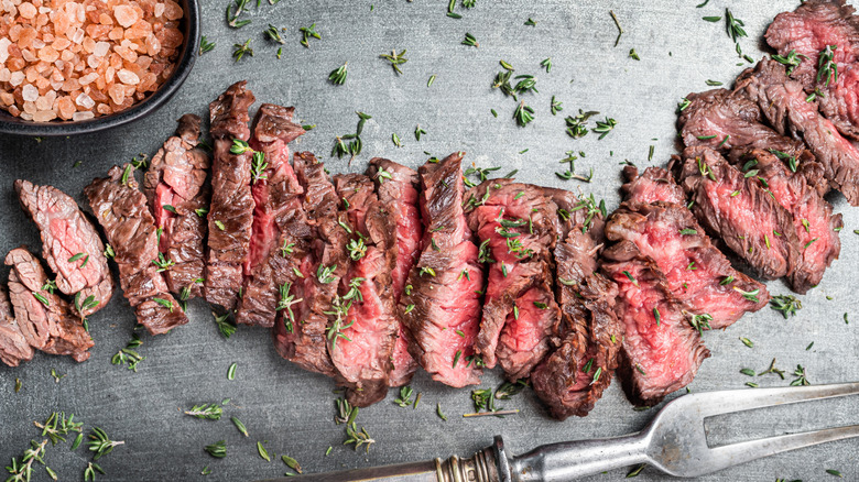 sliced skirt steak on a gray serving plate, with garnishes and herbs