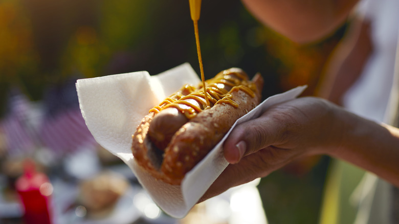 Person putting mustard on hot dog