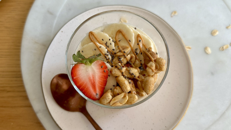 Jar of overnight oats topped with bananas, strawberry slice, peanuts, and peanut butter drizzle