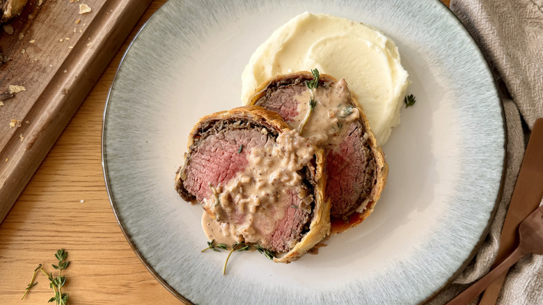 sliced beef wellington with sauce and mashed potatoes