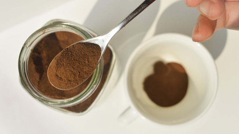 Instant coffee being spooned from a jar into a cup