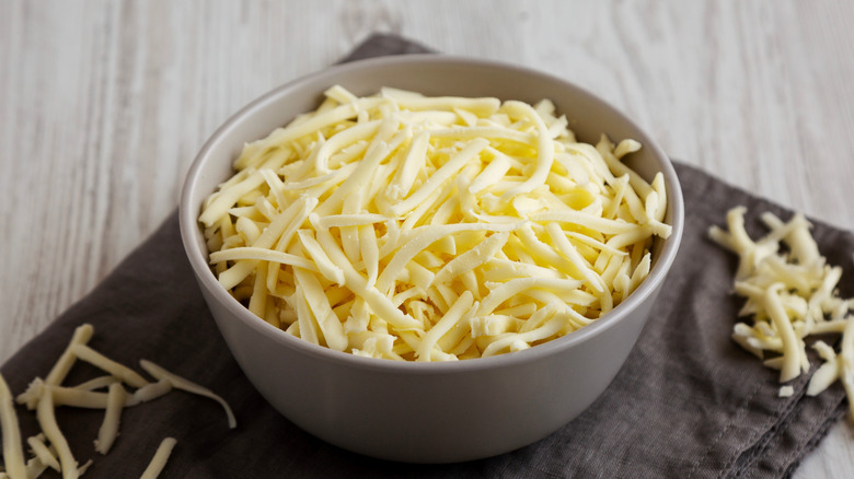 Shredded mozzarella cheese in a white bowl on a black napkin