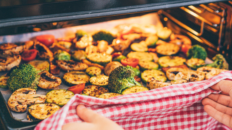 A person pulling a tray of roasted vegetables out of the oven