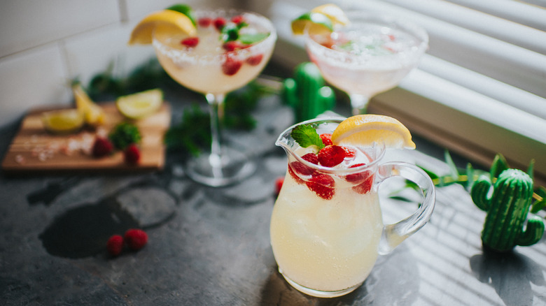 Jug of lemonade with raspberries and two garnished cocktail glasses