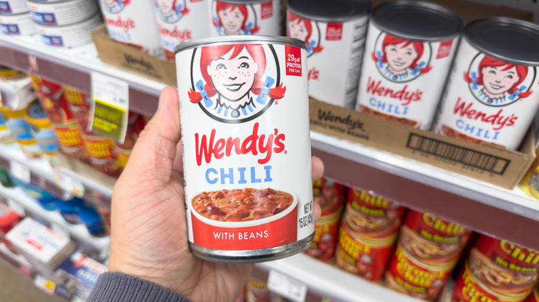 A hand holding a can of Wendy's chili at a grocery store