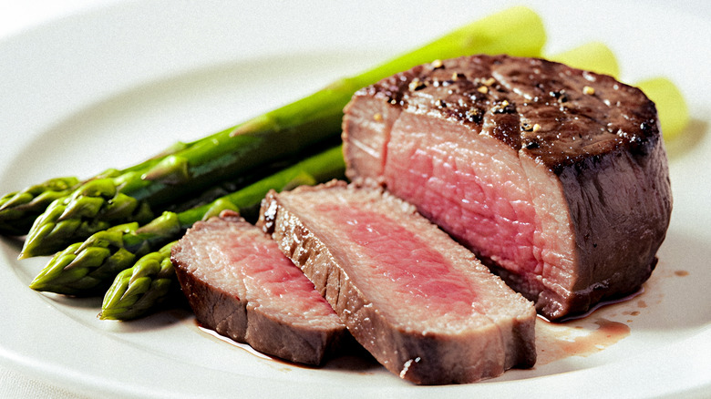 Sliced filet mignon on a plate next to asparagus.