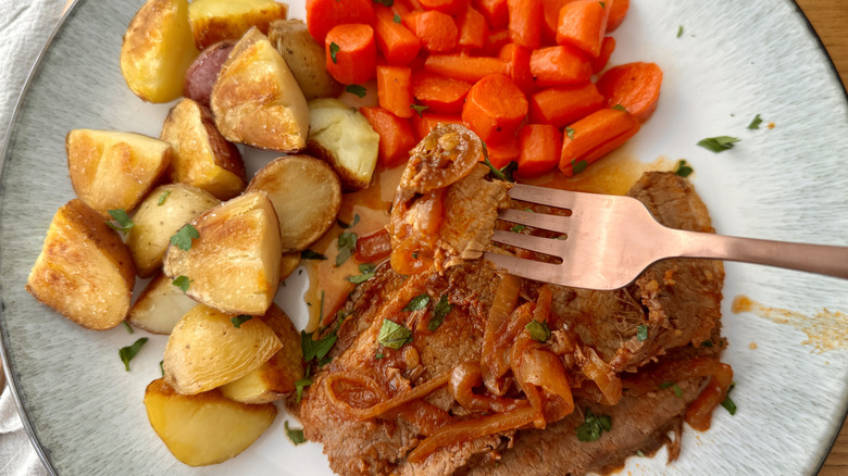 Forkful of Brisket over plate with meat, carrots, and potatoes