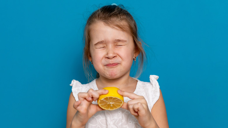 Young girl holding lemon and puckering her face at the sourness