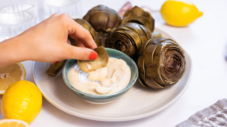 hand dipping artichoke leaf in aioli 