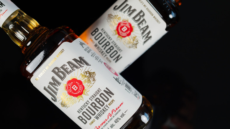 Two bottles of Jim Beam Bourbon Whiskey lying on their sides across each other over a black bar top.