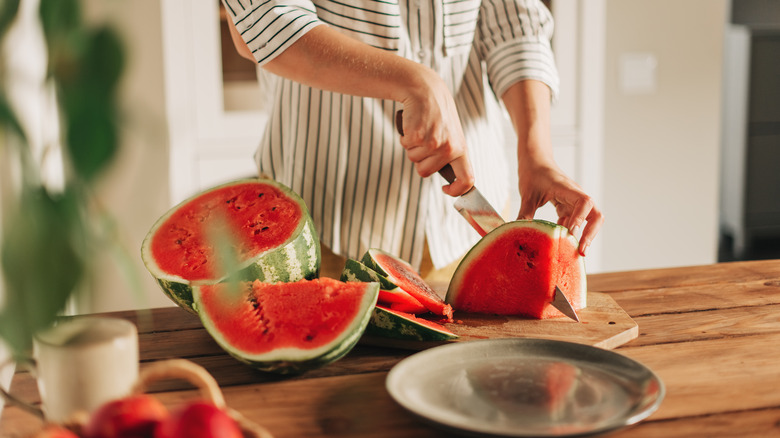 Person cutting a watermelon on a wooden table