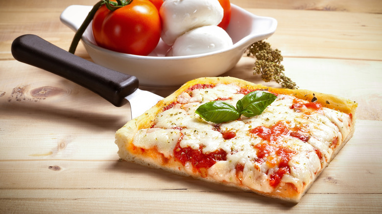 A slice of square pizza al taglio on a spatula.