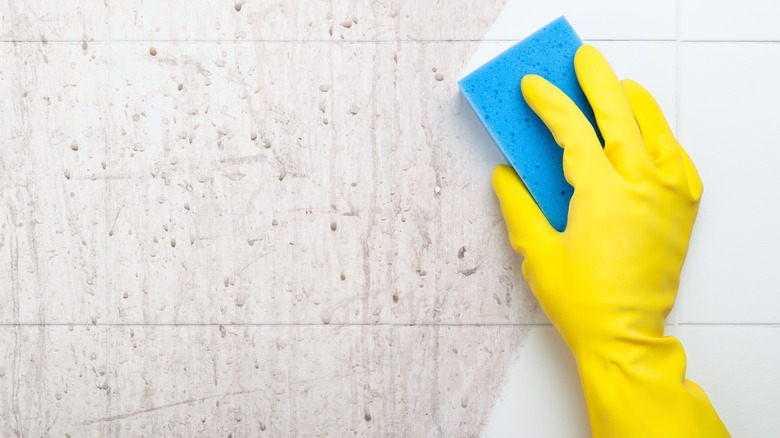 yellow-gloved hand scrubbing dirty wall with sponge