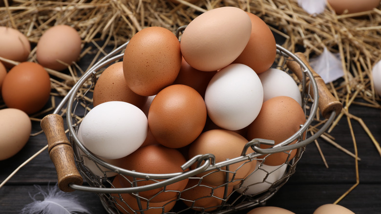 Fresh chicken eggs and dried straw on black wooden table, closeup