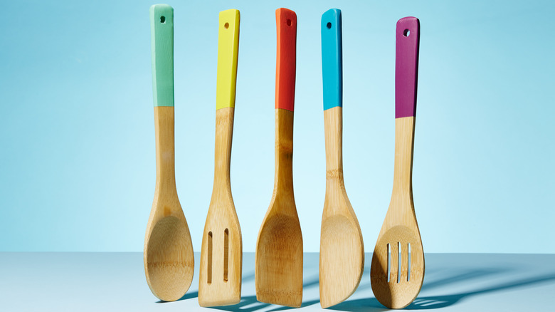 Colorful-handled bamboo kitchen utensils standing upright against a blue background