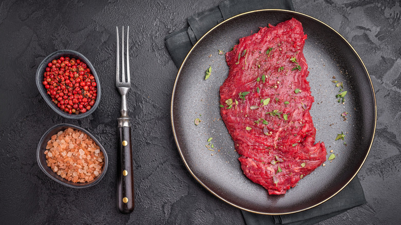 A raw flank steak on a plate with seasonings